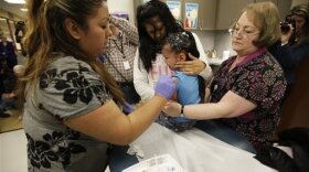 Nurses Fatima Guillen, left, and Fran Wendt, right, give Kimberly Magdeleno, 4, a Tdap whooping cough booster shot.