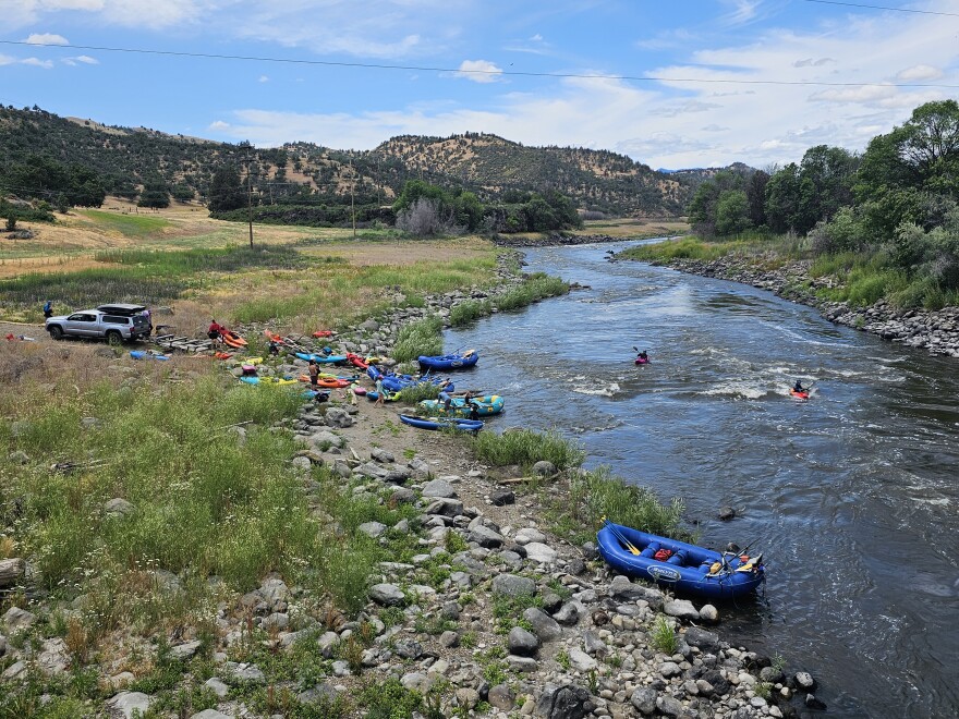 Kayaks and rafts line a rocky shoreline while paddlers launch into a flowing stretch of the Klamath River.