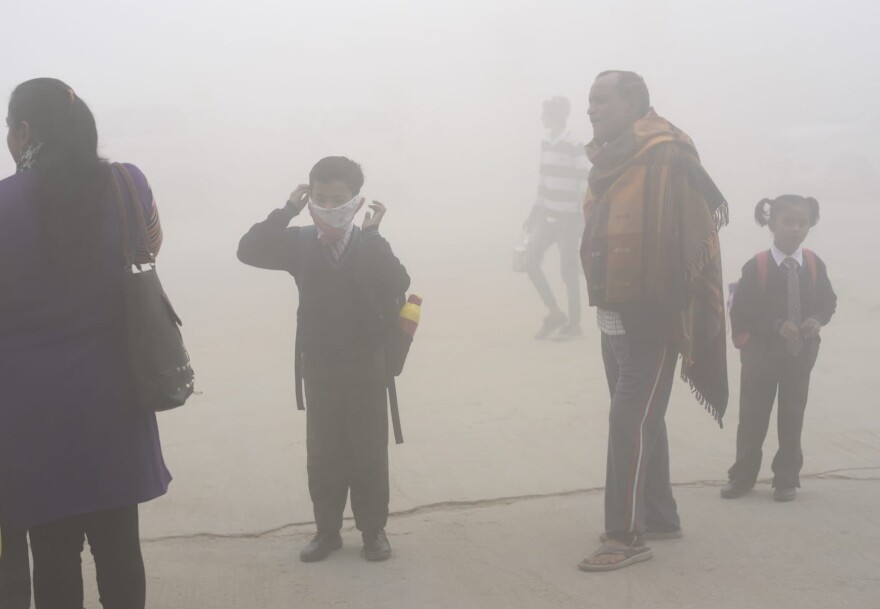 In this Nov. 9, 2017 photo, an Indian boy uses a handkerchief to protect his face as school children and parents await transport surrounded by morning smog on the outskirts of New Delhi, India. (R S Iyer/AP)