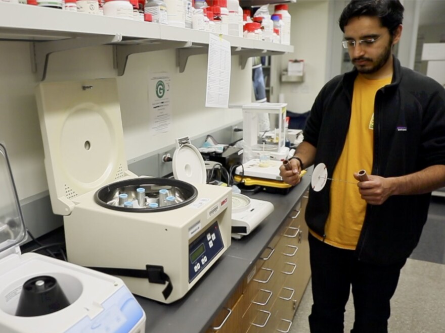 Saad Bhamla holds the paperfuge next to an electrical centrifuge. Both can separate blood samples.