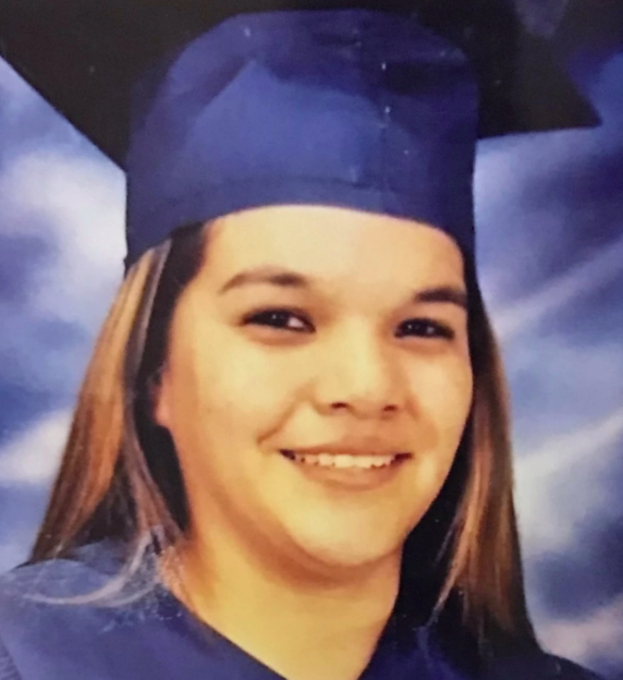 A young woman with long brown hair smiling in a graduation cap and gown.