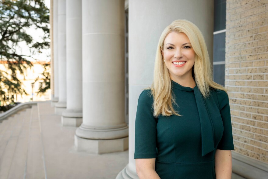 This is an image of Colorado State University President President Amy Parsons standing outside in front of a set of columns on a campus building wearing a dark green dress. 