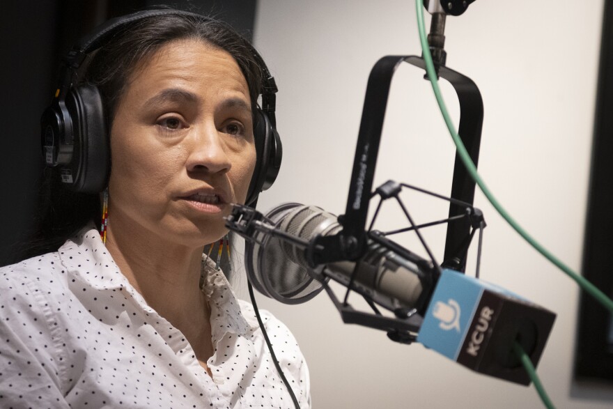 A woman sits inside a radio station talking at a microphone.