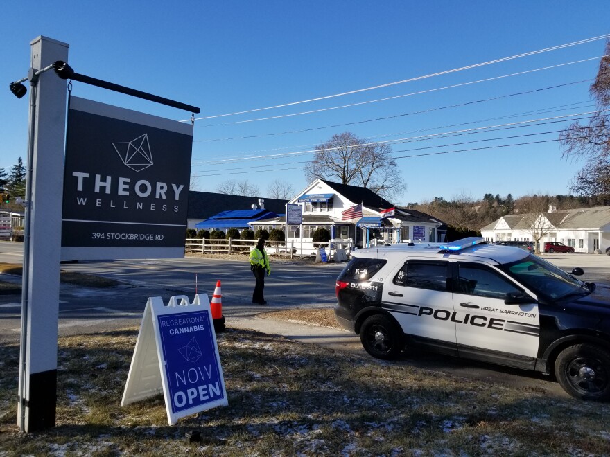 A police SUV is parked outside of signs for Theory Wellness in Great Barrington that declare it open for business.