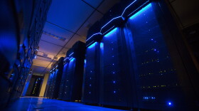 Rows of server banks glow blue inside an otherwise dark data center.