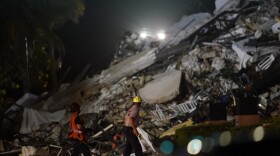 Rescue workers walk beside the rubble as rescue efforts continue where a wing of a 12-story beachfront condo building collapsed Thursday in Surfside, Fla.