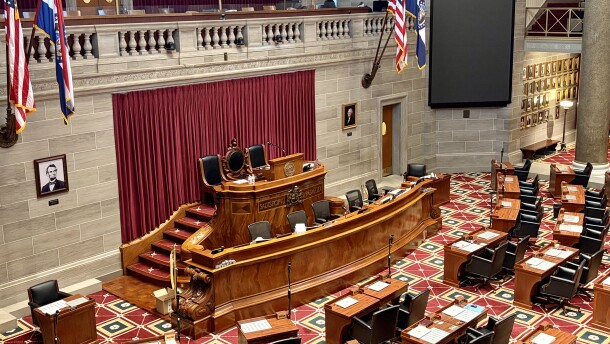 The wooden dais of the Missouri House of Representatives, as viewed from the upper gallery. American and Missouri flags hang from each side. 
