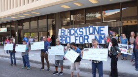 Protesters on Thursday outside the Public Service Company of New Mexico's headquarters hold giant fake checks, made out to PNM and Blackstone executives, detailing their golden parachute compensation guaranteed in the merger agreement between PNM's parent company and the private equity firm Blackstone Infrastructure.
