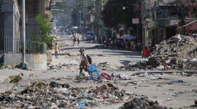 A youth crosses a street littered with garbage in downtown in Port-au-Prince, Haiti, Tuesday, Jan. 20, 2026. (AP Photo/Odelyn Joseph)