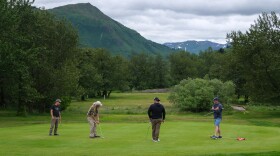 Four golfers wrap up their rounds on a putting green near the entrance.