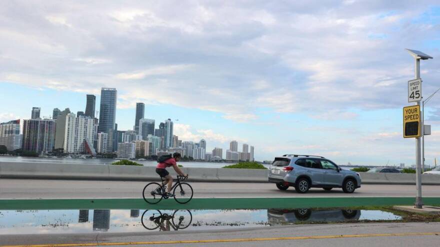 A biker rides near the spot where two cyclists were killed a day earlier, on May 15, 2021, at the foot of William Powell Bridge on the Rickenbacker Causeway. The pair were struck by a car on a roadway that has been dangerous, sometimes deadly, for cyclists.