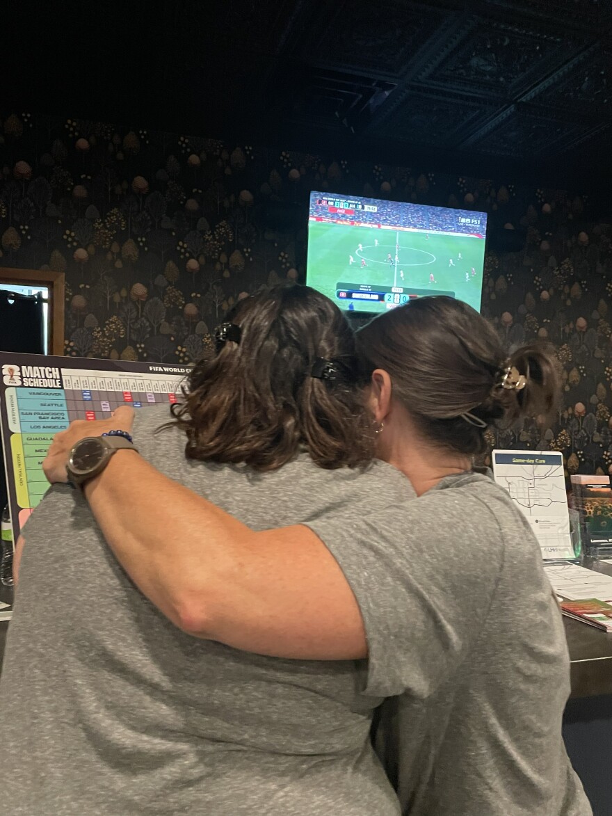 Kim Anspach and Megan Poindexter embrace as they watch the second half of Algeria’s match with Switzerland in the Explore Lawrence lobby. Algeria lost 0-2 and was eliminated from the tournament.