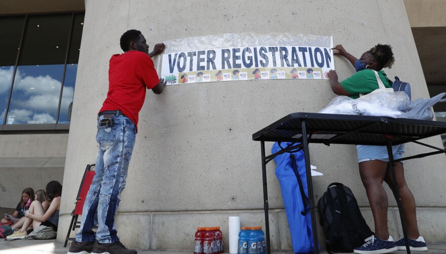 Two people put up a voter registration sign. 