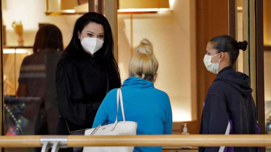 A worker at the Louis Vuitton store, left, wears a protective face mask as she talks to customers at the International Mall Wednesday, May 6, 2020, in Tampa, Fla. Twenty percent of the stores were operating when the mall reopened, with more to follow later in the day. The mall is taking active measures to help stop the spread of the coronavirus. (AP Photo/Chris O'Meara)