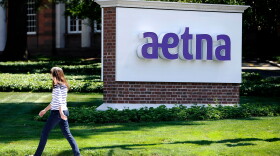 In this Tuesday, Aug. 19, 2014 file photo, apedestrian walks past a sign for health insurer Aetna Inc., at the company headquarters in Hartford, Conn.