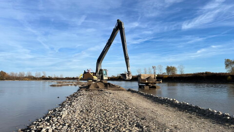 A dump truck and an excavator unload sand on a stony barrier island in the Sandusky Bay.