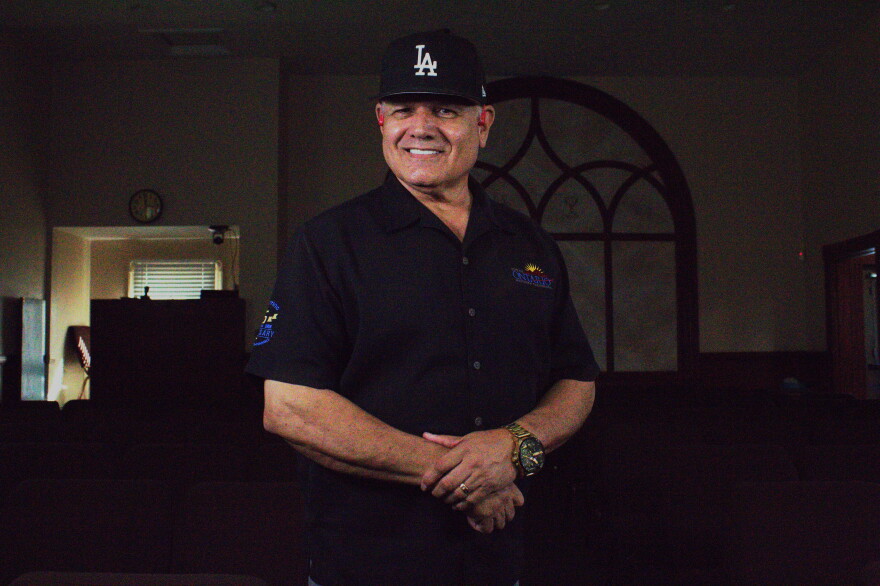 A man stands in the middle of a dimly lit church with hands together at his torso 