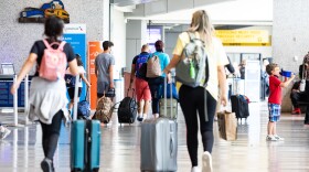 Crowds of passengers, some wearing protective face masks, line up before passing through a TSA security check point within the Austin-Bergstrom International Airport main terminal