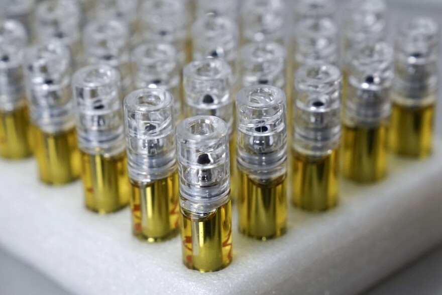 Vape cartridges containing THC oil are arranged in a triangular pattern on a tray. They look like small, plastic tubes filled with golden liquid. 