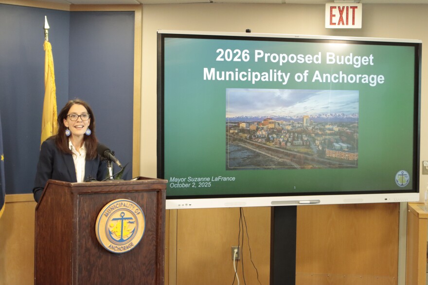  a woman in glasses speaks next to a screen