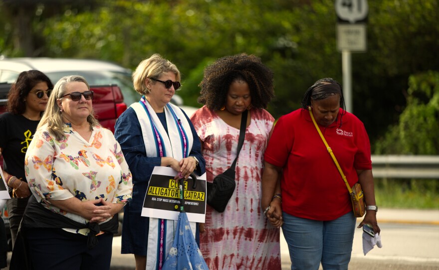 Audrey Warren from First Miami United Methodist Church holds a 'Close Alligator Alcatraz" sign while flanked by other prayer vigil attendees at Sunday's eighth prayer vigil across from the entrance to the detention center on Sept. 21, 2025.