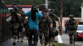Police wearing riot gear walk toward a man with his hands raised Aug. 11 in Ferguson, Mo. Renewed calls for police departments to hire more minorities have followed the shooting there of a black man by a white police officer.
