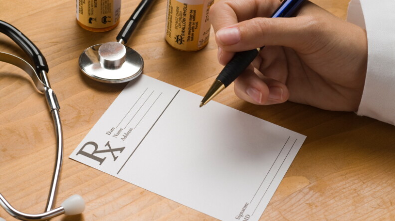 A doctor holds a pen over a prescription pad. 