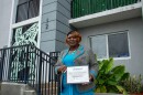 Beatrice Regina Thomas stands in front of the redeveloped Liberty Square, holding a certificate in Entrepreneurship awarded by Related Group and The Miami-Dade Chamber of Commerce.