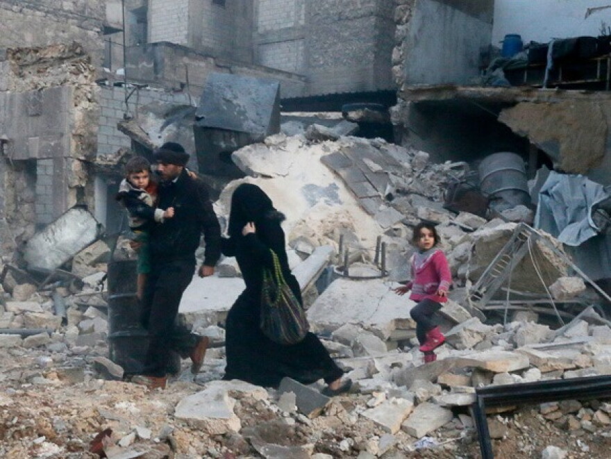 People walk on rubble of collapsed buildings at a site hit by what activists said was barrel bombs dropped by government forces in Aleppo's Dahret Awwad neighborhood January 29, 2014.