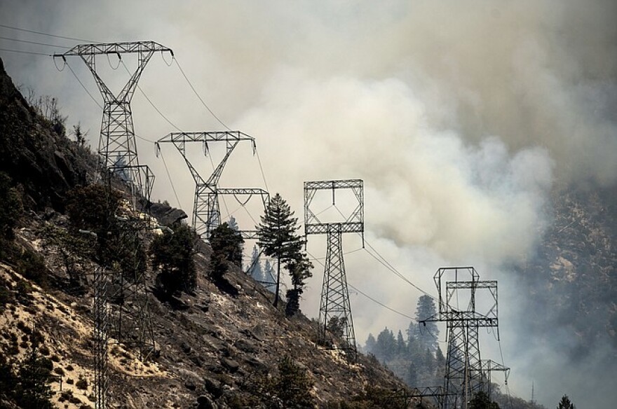 Smoke billows behind power lines as the Dixie Fire burns along Highway 70 in Plumas National Forest, Calif., on Friday, July 16, 2021.