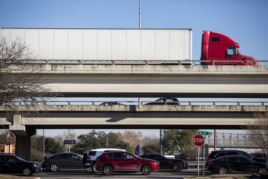 A ground level view of the upper decks of I-35 as seen while standing on 39th Street facing east. The perspective is set up so that three levels of vehicles are visible. The ground level frontage roads, the northbound main lanes and the closer southbound main lanes above that.