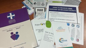 Pamphlets, business cards, and general information about McLean County and national mental health and substance use services are spread on a table.