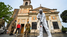 A member of the Italian Army, wearing protective overall and mask, sprays sanitizer outside of the Santuario della Madonna del Divino Amore church on May 13, 2020 in Rome during the country's lockdown. (Andreas Solaro/AFP/Getty Images)