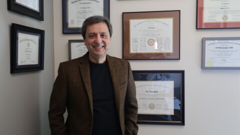 Dr. Ali Hammad stands in front of a wall in his office. The wall has framed diplomas and certificates.