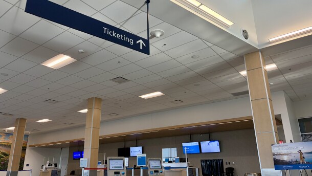 A wide shot of the American Airlines ticketing counter at the Columbia Regional Airport. A navy blue rectangular sign hangs from the ceiling and says "Ticketing"