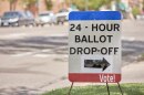 A red, white and blue sign that says "BALLOTT DROP-OFF" with an arrow sits on the side of a street.