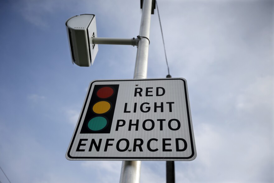 FILE - A red light photo enforcement sign is seen below a red light camera Tuesday, Dec. 16, 2014, in Lawrence Township, N.J. (AP Photo/Mel Evans)