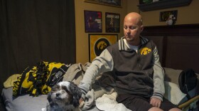 Jon Miller sits in his bedroom with his dog, Carlos, whom he received as a present for successfully completing cancer treatment a decade ago. Miller sustained severe brain damage, and requires the help of home health aides to continue living in his home.