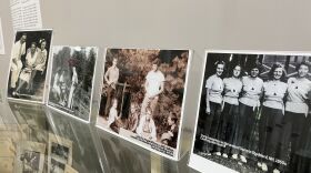  Black and white and sepia photos arrayed on a glass countertop show images of campers at various summer camps. 