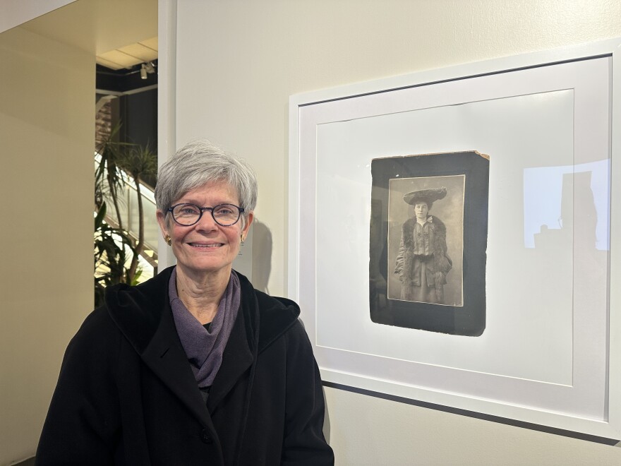 Patricia Watkins stands next to a portrait photograph of Catherine Higgins Watkins, her great-grandmother who was institutionalized at the Buffalo State Asylum.