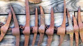 A row of rusty red pick axes sits against a dull wood background.