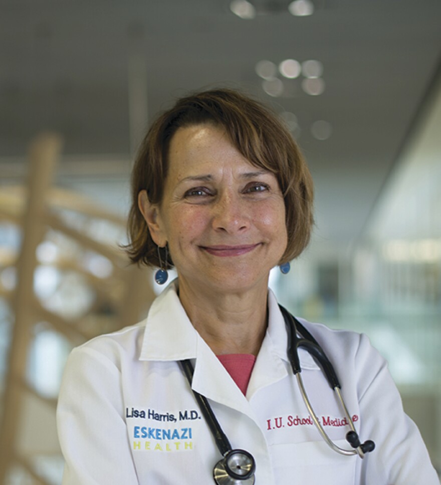 A woman smiling at the camera wearing a white coat and stethoscope.