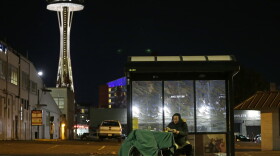 In this Oct. 30, 2017 photo, Dave Chung, who says he has been homeless for five years on the streets of California and Washington state, eats a meal before bedding down in a bus shelter in view of the Space Needle in Seattle. Chung says he has been offered shelter many times, but chooses to remain outside due to the living conditions in homeless shelters and conflicts he has with other people. (AP Photo/Ted S. Warren)