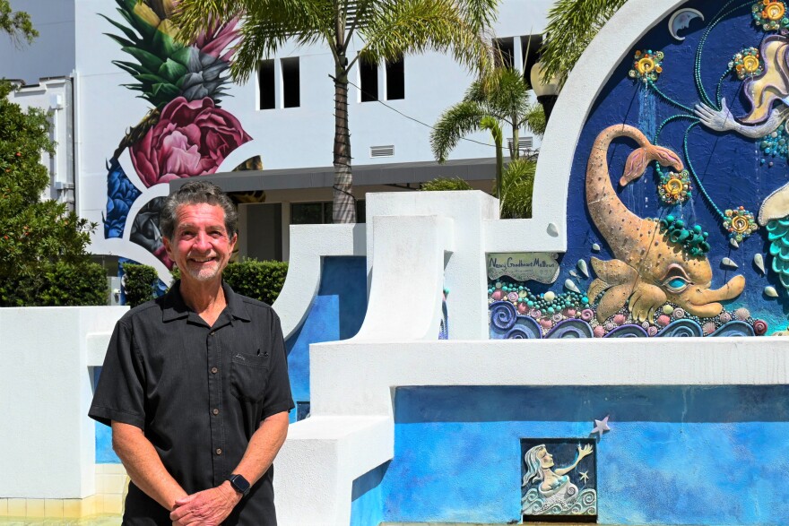 Man standing, smiling in front of a colorful sign