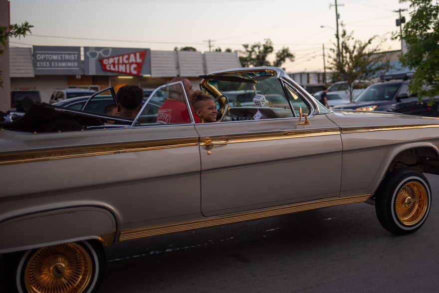 A kid smiles wide as he gets a ride on the 1962 Impala, glistening with the gold chrome.