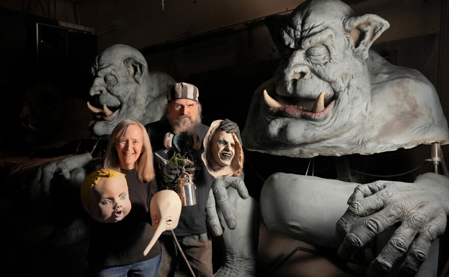Ed and Marsha Edmunds hold several Halloween masks and stand next to two Colossus monster figures