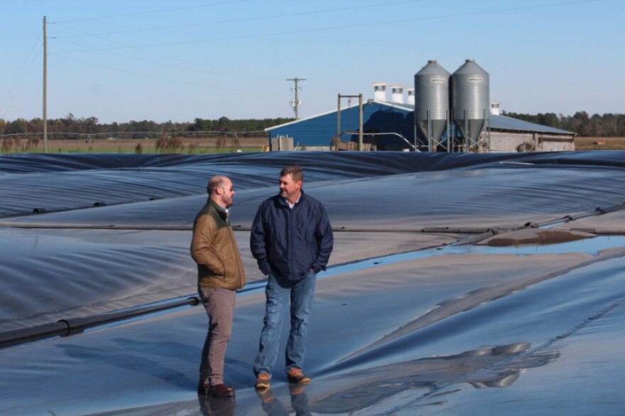 Ryan Childress (left), Dominion Energy's director of gas business development, and Kraig Westerbeek, an executive at pork producer Smithfield Foods, stand on a plastic-covered manure pond in North Carolina.