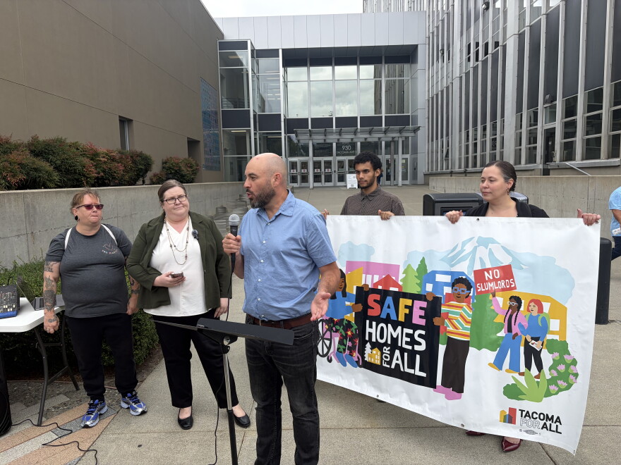 People stand at a press conference in front of a Tacoma court house. They have a banner that reads "Safe Homes For All" 