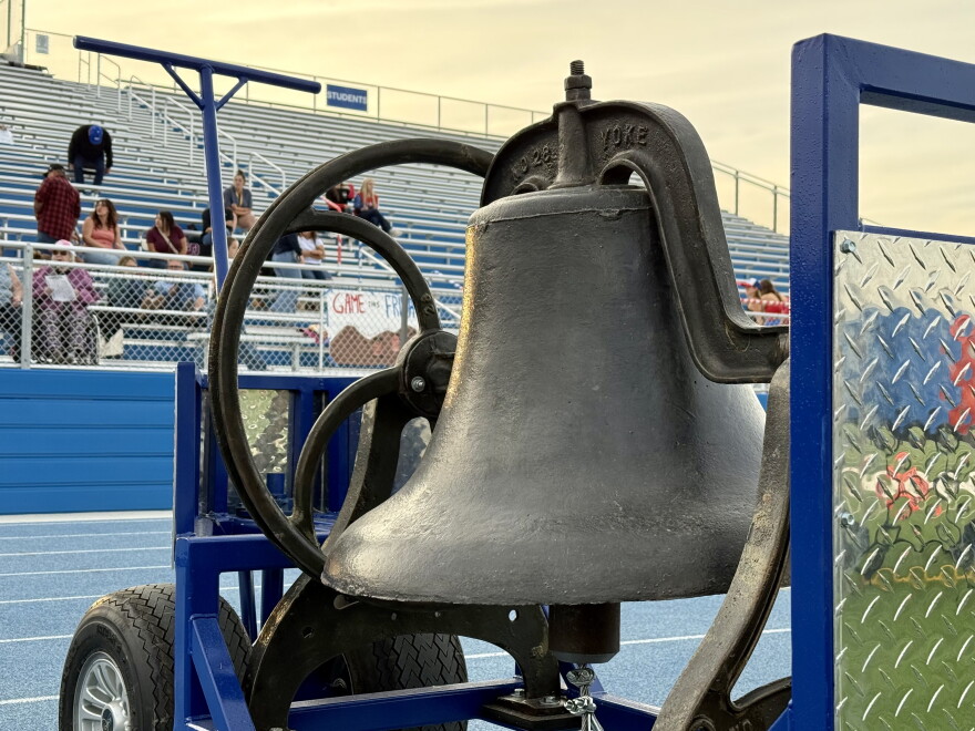 A big iron bell, mounted to a blue metal cart, sits on the track at Walla Walla High School's Blue Devil Stadium.