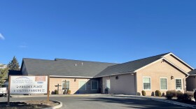 A one-story beige building with a parking lot in front. A sign on the left says "Klamath Basin Behavioral Health, Phoenix Place (arrow pointing to the left), Visitor parking (left or right)"